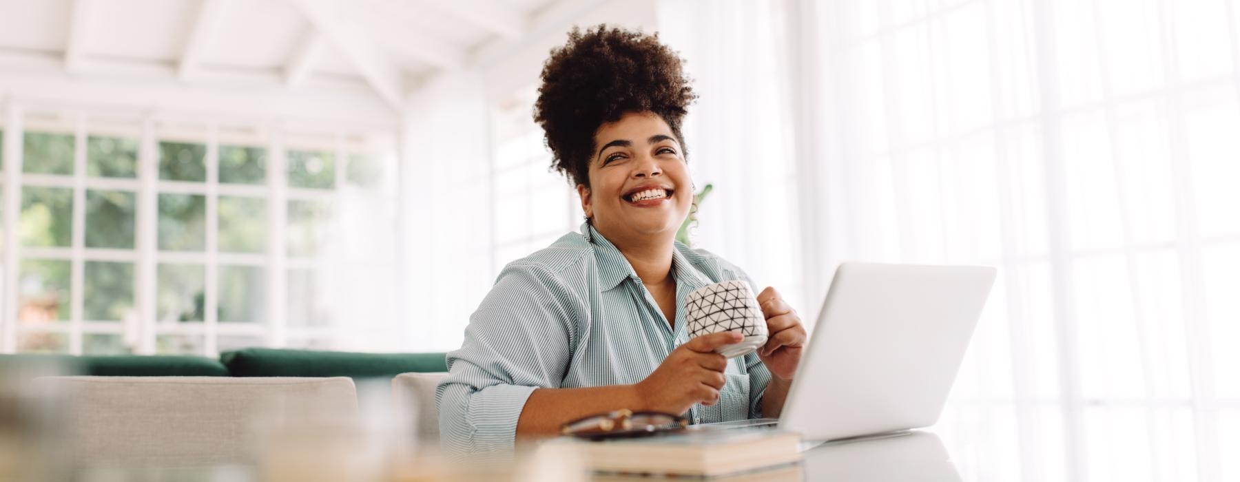 woman sits in front of her laptop with a mug in her hands